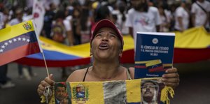 Ein Mann mit der Fahne Venezuelas und Fotos des früheren Präsidenten Chavez
