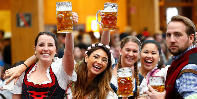 Mehrere Frauen und ein Mann in Trachtenkleidung- sie heben Biergläser in die Höhe