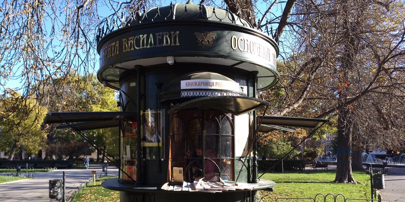 Ein kleiner runder Kiosk in Form einer Litfasssäule steht im herbstlichen Sonnenlicht