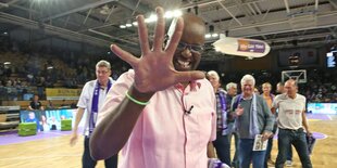 Wilbert Olinde in einer Sporthalle, hält seine Handfläche in Richtung Kamera