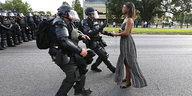 Eine junge schwarze Frau reicht Polizisten die Hand. Hinter ihnen stehen viele andere Polizisten.