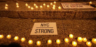Teelichter stehen auf Treppenstufen, daneben Schilder mit der Aufschrift "NYC strong" und "Standing with Muslims against islamophobia and racism"