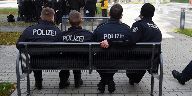 Vier Polizeischüler sitzen mit dem Rücken zum Betrachter auf einer Bank