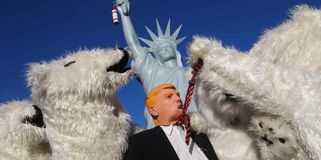 Eine Trump-Impersonator, eingerahmt von Eisbären, dahinter die Freiheitsstatue