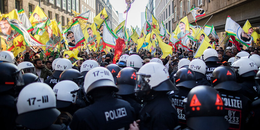 In einer Straße: im Vordergrund eine Polizeikette, dahinter Demonstranten mit gelben Fahnen