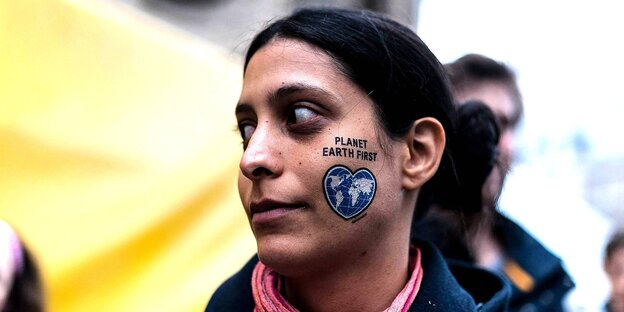 Frauengesicht mit einer gemalten Erde auf der Backe: Planet Earth First