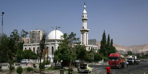 Im Hintergrund ist eine Moschee. davor steht ein Autowrach auf einer beschädigten Straße in Damaskus.