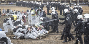Polizisten und weiß gekleidete Demonstranten, ein Polizist sprüht Pfefferspray auf eine Gruppe sitzender Demonstranten