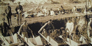 Menschen mit Schubkarren vor einem Graben