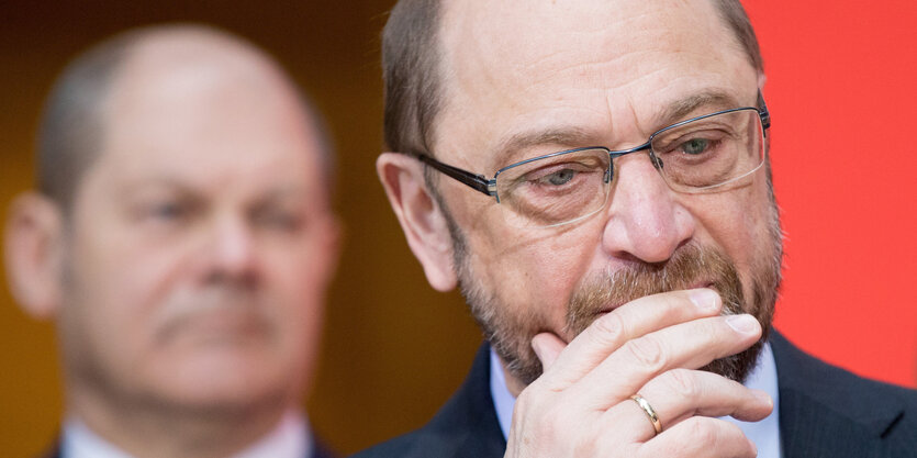 Ein Mann mit Brille guckt nachdenklich, im Hintergrund sieht man einen weiteren Mann