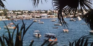 Blick auf eine Bucht mit Booten, Schatten von Palmenblättern sind am Uferrand zu sehen