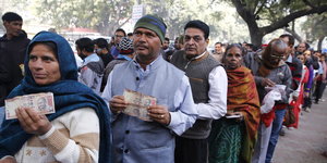 Indische Frauen und Männer stehen, wertlose Banknoten haltend, in einer Schlange