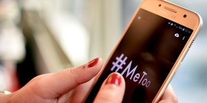 Eine Frau hält ein Smartphone in der Hand, auf dem Display steht der Hashtag Me too
