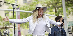 Miley cirus steht auf einer Bühne, breitet ihre Arme aus und steckt die Zunge heraus