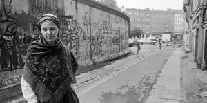 Eine Frau steht vor einem Stück der Berliner Mauer