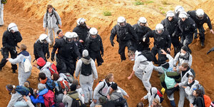 AktivistInnen in weißen Anzügen stehen vor und hinter einer Polizeikette