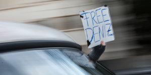 Eine Person hält aus einem fahrenden Auto ein Schild. Darauf steht „Free Deniz“