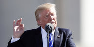 Donald Trump kneift das Gesicht, sowie Daumen und Zeigefinger seiner rechten Hand zusammen und spricht in ein Mikrofon