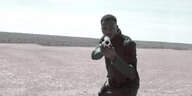 in einer öden Landschaft zielt ein Mann mit einer großen Pistole in Richtung des Betrachters