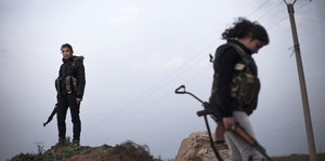zwei kurdische Kämpferinnen stehen vor suppig-grauem Himmel auf einem Hügel