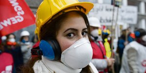 Eine Frau mit Helm, Atemschutz und Kopfhörern protestiert gegen den schlechten Zustand einer Berliner Schule