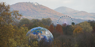 Eine große Weltkugel und ein Riesenrad vor herbstlichen Hügeln