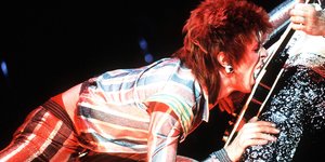 David Bowie mit Rothaar-Frisur beißt in eine Gitarre