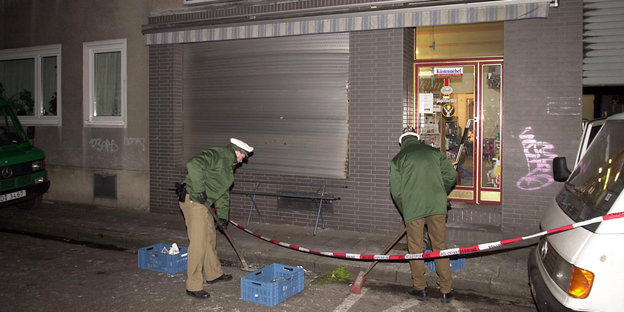 Zwei Polizisten fegen vor einem Laden mit heruntergelassenem Rollo