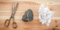 Eine Schere, ein Stein und ein zerknülltes Blatt Papier liegen nebeneinander