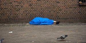 Ein Mensch liegt in einem Schlafsack auf dem Gehweg