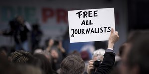 Ein Mensch steht in einer Menschenmenge und hält ein Schild mit der Aufschrift: Free all Journalists