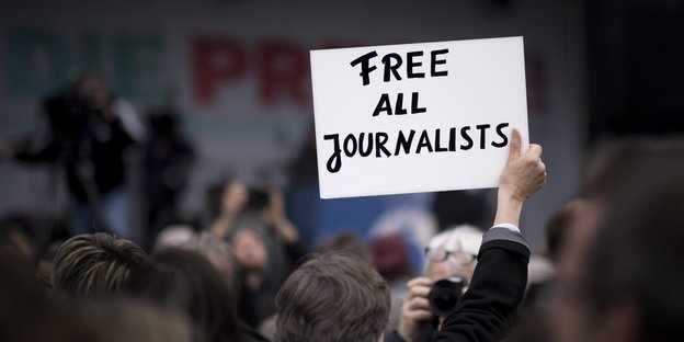 Ein Mensch steht in einer Menschenmenge und hält ein Schild mit der Aufschrift: Free all Journalists