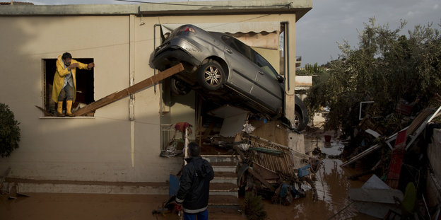 Männer versuchen, ein silbernes Auto zu beseitigen, dass von Sturm und Wassermassen in den Eingang eines Hauses gespült wurde