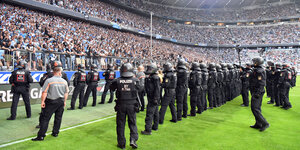 Drei lange Polizeiketten stehen auf dem Rasen des Stadions und schauen in die Ränge der Löwen-Fans von München 1860.