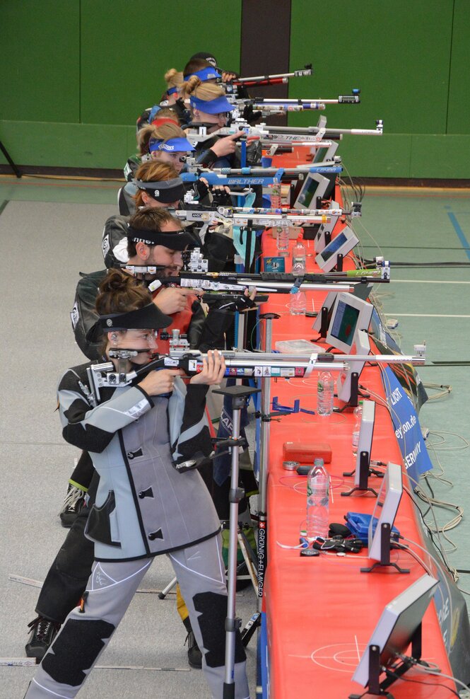 Sieben Menschen zielen mit ihrem Sportgewehr am Schießstand