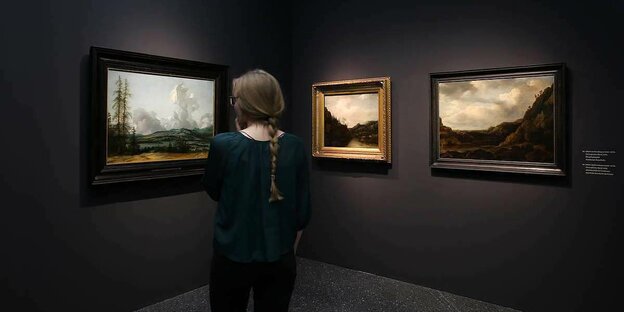 Eine Frau betrachtet Gemälde des Goldenen Zeitalters in einer Kunstausstellung
