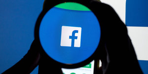 Das Icon der Social Media-Plattform Facebook ist auf einem Handy durch eine Linse zu sehe