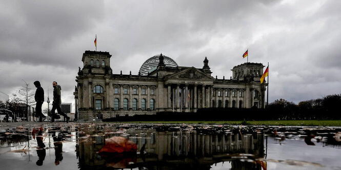 Eine Pfütze vor einem Gebäude. Es sind dichte Wolken am Himmel