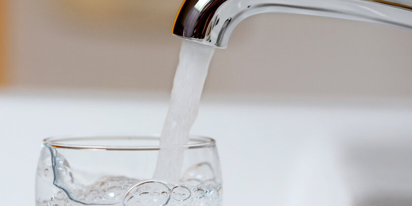 Wasser fließt durch einen Hahn in ein Glas