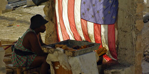 Eine Frau sitzt vor einer Schale mit Essen, dahinter weht eine US-Fahne