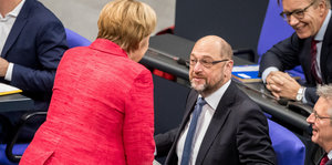 Merkel im magentaroten Sakko steht vor dem sitzenden Martin Schulz, der zu ihr aufsieht