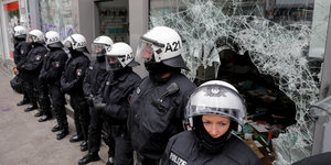 Polizeibeamte mit weißen Helmen stehen vor einer zersplitterten Fensterscheibe