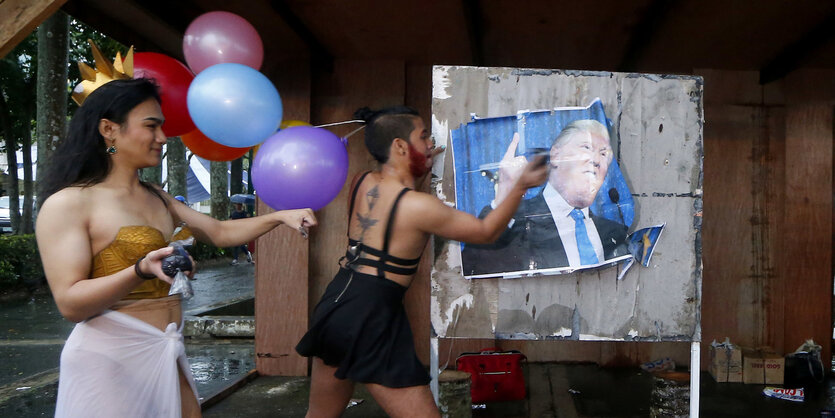 Zwei Mitglieder der LGBT-Community verschmutzen aus Protest ein Plakat von Donald Trump.