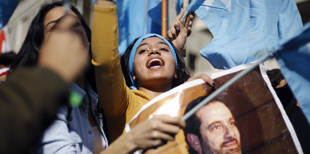 Ein Mädchen ruft Slogans, andere halten Fahnen und Bilder von Saad Hariri in den Händen