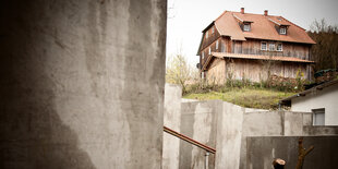 Betonstelen im Vordergrund, dahinter ein rustikales Holzhaus