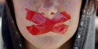 Der Mund einer Frau mit mit einem roten Kreuz zugeklebt.