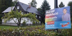 Ein AfD-Plakat von Tino Chrupalla steht neben einem Haus