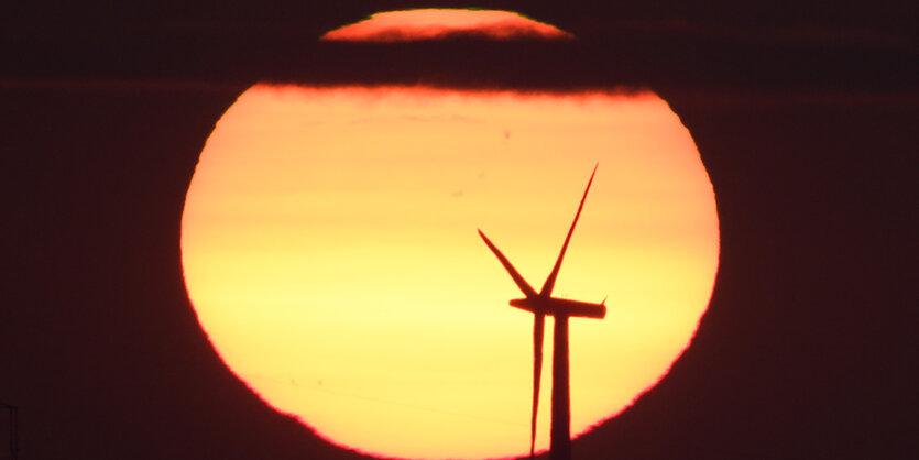 Vor dem hell leuchtenden Mond ist die Silhouette einer Windkraftanlage zu sehen