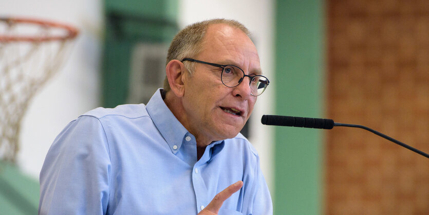 Mann mit Brille an Mikrophon, hinter ihm ein Basketballkorb