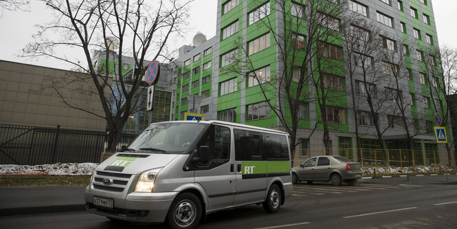 Ein graues Auto mit grünem Streifen auf dem die Buchstaben R und T stehen vor einem grau-grünen Haus